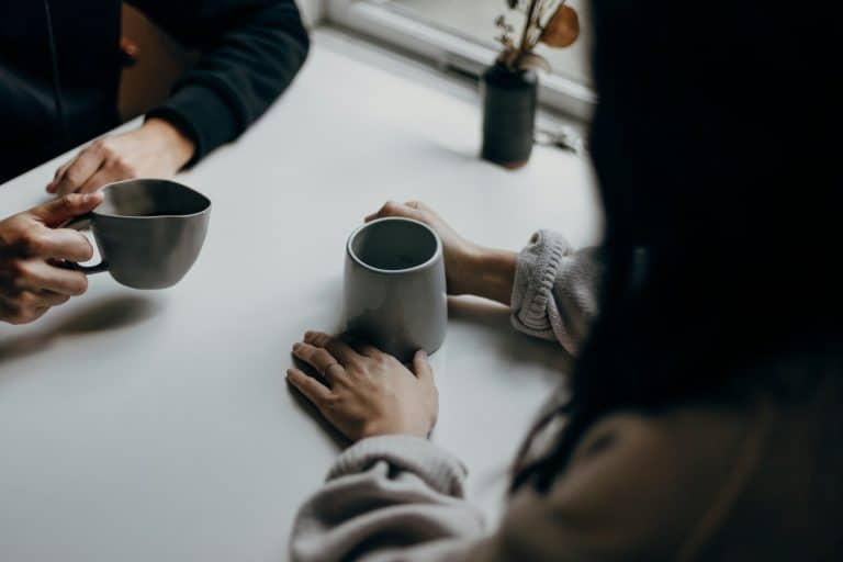 Couple holding coffee mugs and talking at the table