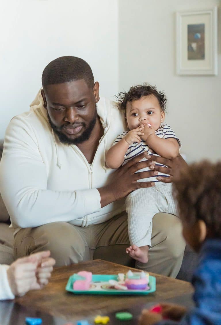 Father holding his baby while playing with his children at home