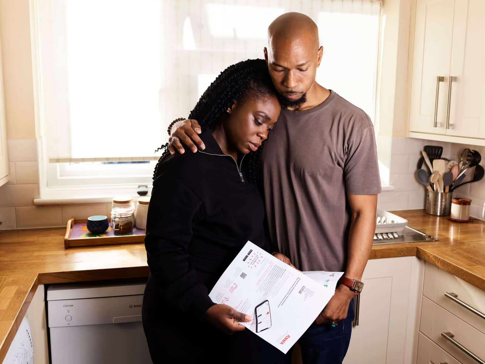 Husband holding and comforting his wife in the kitchen while she leans on him