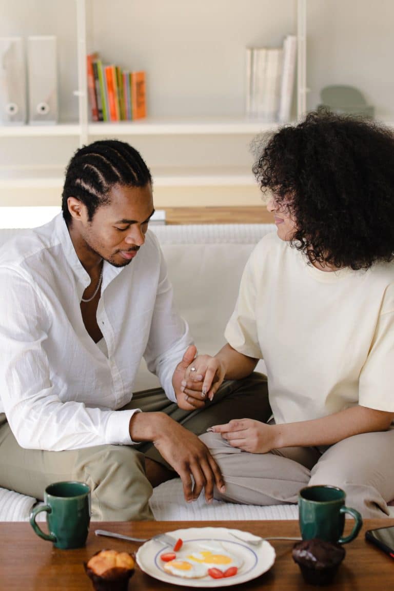 Couple holding hands while sitting close together on a couch at home