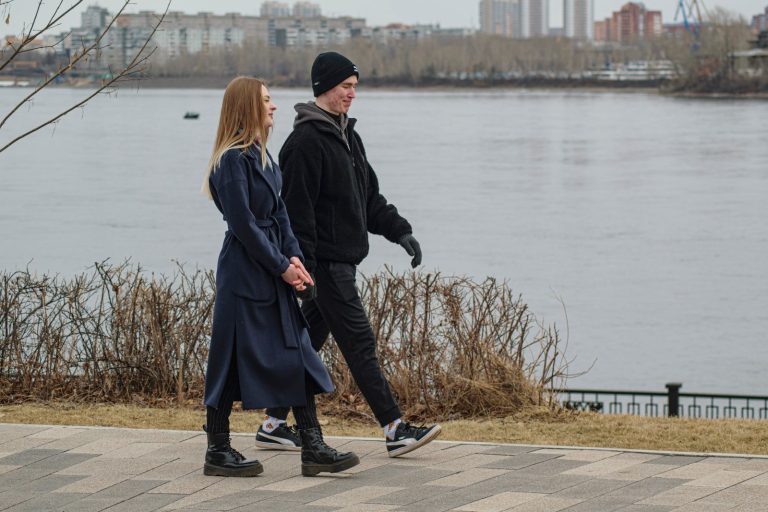 Couple in winter coats holding hands on a winter walk by a snowy waterfront