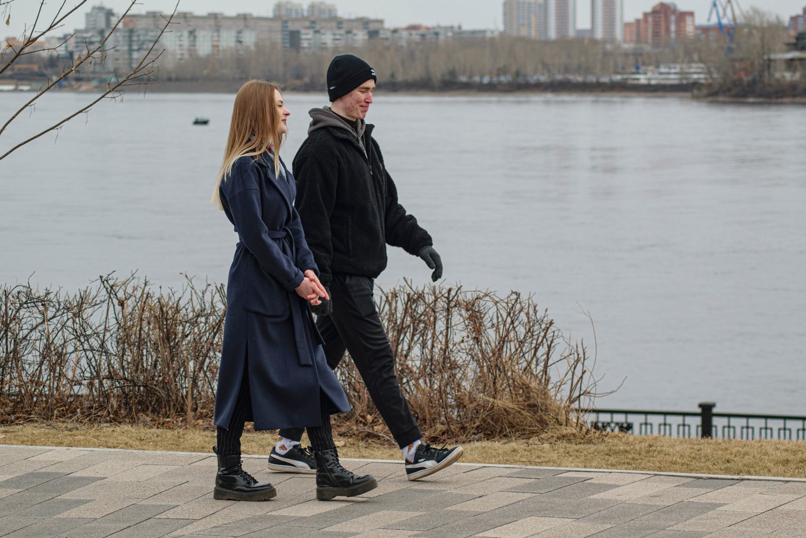 Couple in winter coats holding hands on a winter walk by a snowy waterfront